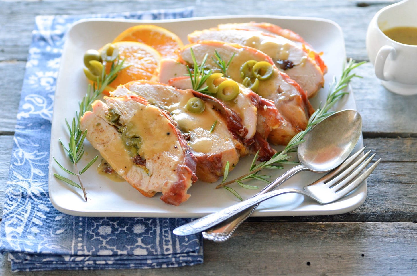 slices of prosciutto wrapped stuffed turkey breast with gravy on a plate, and the plate is sitting on a wood table.