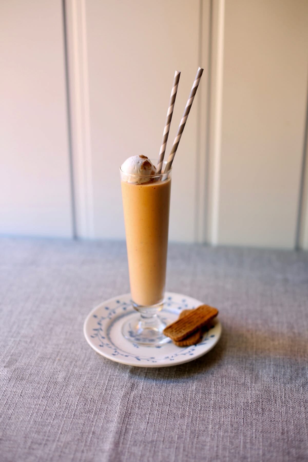 an orange colored milkshake in a tall glass with a small plate with two graham crackers, sitting on a gray table. 