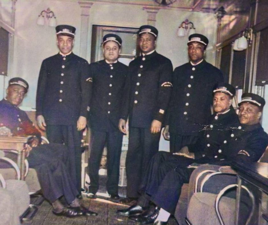 A group of Black Pullman porters wearing formal railway uniforms pose together inside a train car in the early 20th century. Their expressions are dignified and composed, symbolizing unity and professionalism amid segregation-era labor conditions.