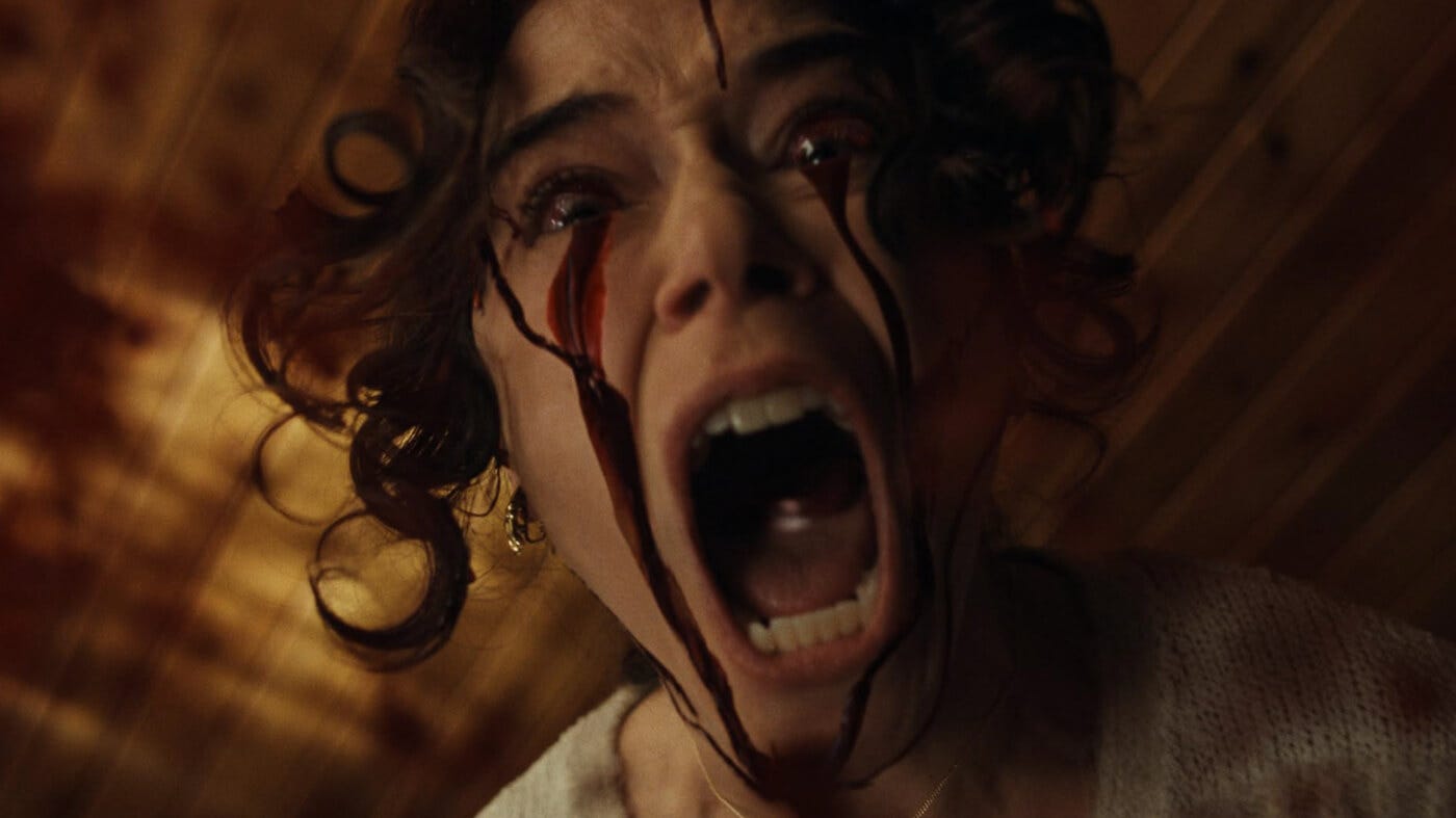 A woman screams in horror as blood pours from her eyes, trailing dramatically down her cheeks, as she looks down at the camera.