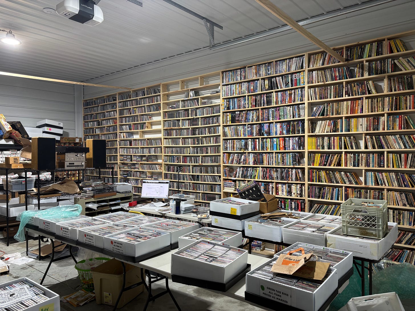 An angled view of one wall of Keith's warehouse, with ten-foot-high shelves full of CDs, boxes of more music on tables in the foreground, and Keith's computer and shipping station in between