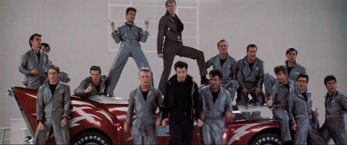 The Greasers with their treasured car Greased Lightning in the workshop - publicity still from 1978 film Grease