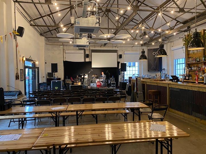 Inside a big warehouse style venue with stage and musical equipment. Stef from Pukka PA Hire setting up
