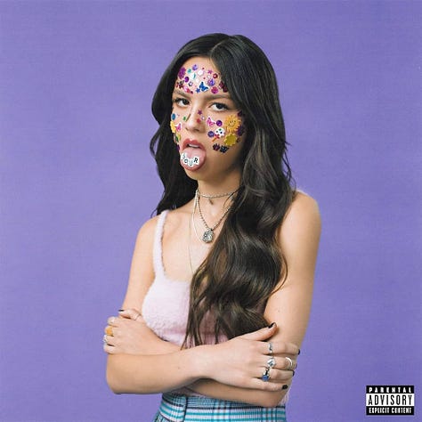 1: A close cropped photograph of a model with dark, bob-length hair against a white background. The model’s eyes are closed, her head tilted up, and her mouth is in an open smile. The model’s face, neck, and visible clothing are covered in an assortment of stickers. 2: A simple illustration in black and white showing a circle that contains smaller half-circles pressed up against one another. The caption reads: “Mosaic of subcultures.” 3: A grainy photograph showing a teenager dressed in baggy jeans and a black t-shirt standing on her bed against two walls filled with posters for bands, rockstars, and other celebrities. One prominent poster is for the band Alice in Chains. 4: A photograph of a pink and white flip phone, surrounded by an assortment of phone charms, including Hello Kitty charms, anime figurines, plush toys, and lip gloss. 5: A young person sits backwards in a chair, turned away from the camera. His face, arms, and back are adorned with star stickers, which shine in the light. 6: A screenshot of a listing on Ebay. The image in the listing shows three closed notebooks laid flat on top of each other. Below the image, a caption describes the listing as “Handwritten Diary, Troubled Teenager, 2000’s.” Below the caption the price read $56. Below the price the listing says 6 bids, Ends in 5 days and 7 hours. 7: The cover of Olivia Rodrigo's debut album Sour. Olivia Rodrigo is standing against a purple backdrop, wearing a fuzzy pale pink tank top and checkered bottoms. She looks at the camera and sticks out her tongue. On her tongue, letters spell out the word “Sour.” Her face is covered in an assortment of stickers. 8: Photograph of a group of four teenage girls posing in front of a white building during an annual U.F.O festival. They are each wearing a matching blue and white striped summer dress, a tiara, a pair of silver alien sunglasses, antennas, and a sash embroidered with the year (2023) and the phrase “Hudson Ambassador” along with their name, written in cursive. 9: A single speaker stands on a stage in front of a crowd almost entirely obscured in darkness. Behind the speaker, a large white screen displays the words: “turn customers into fanatics, products into obsessions, employees into ambassadors, and brands into religions.” The text is all lowercase and in black, but the words fanatics, obsessions, ambassadors, and religions appear in various shades of blue for emphasis.