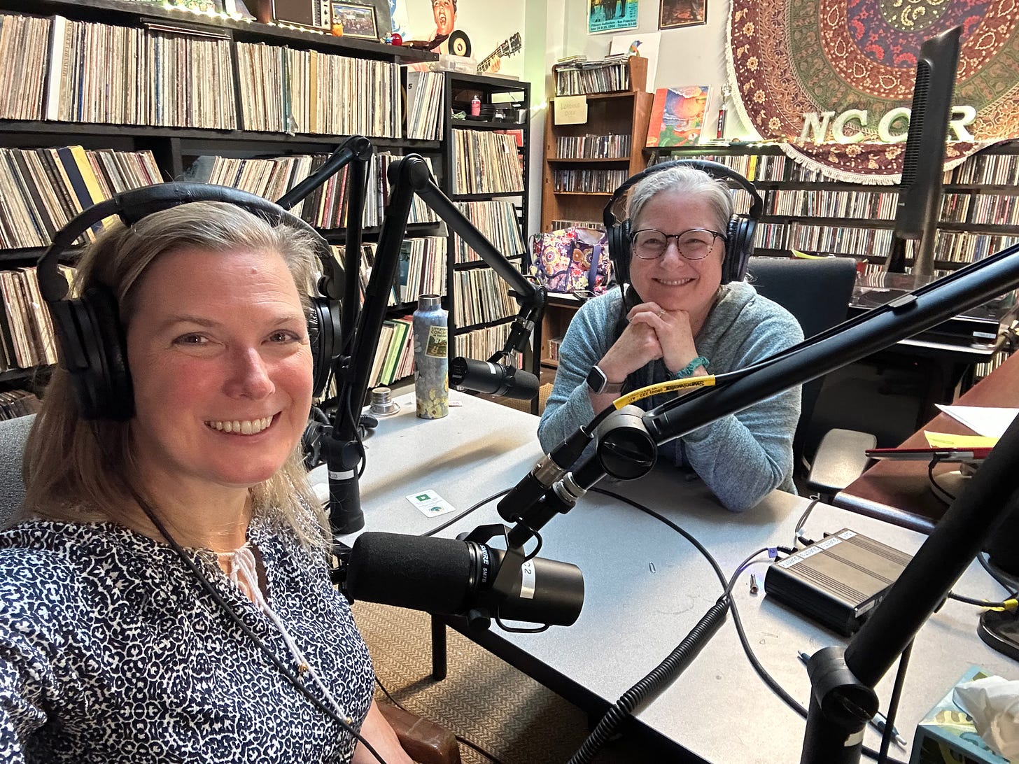 Liz and Meggen sit at microphones with headphones on