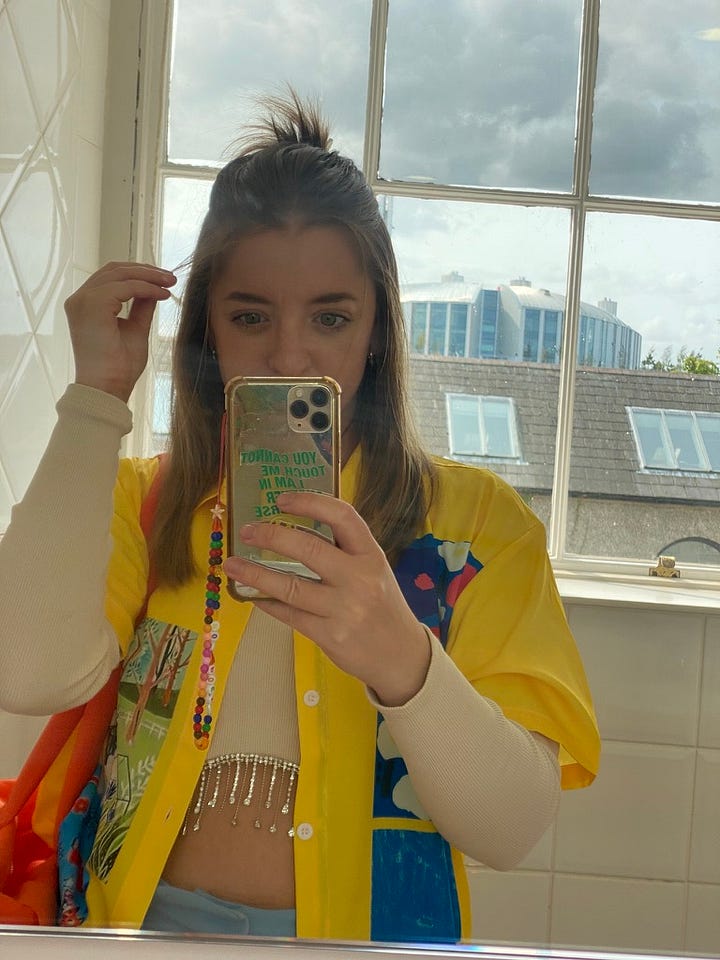 Left: Kelly in a yellow patchwork short sleeve button-up layered over a long-sleeve beige crop top with rhinestone tassels. Right: Kelly in a silky multicolored top and flame-shaped sunglasses.