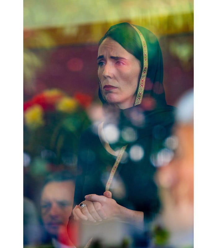 Fabulous and famous picture of Jacinda Ardern, wearing a head covering and looking grief-stricken; taken through a stained glass window.
