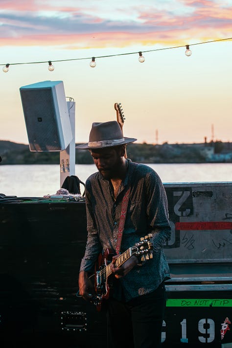 A collage of five photos of Gary Clark Jr. performing outdoors. The images are a mix of color and black and white, featuring close-ups of his face as he sings and wider shots of him playing the guitar, all while wearing his signature hat.