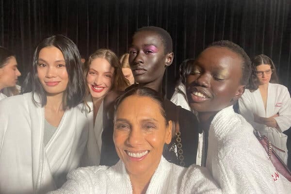 Backstage at the Carolina Herrera show, Ming Smith, in the center of a diverse group of models, smiles broadly for the camera, They’re all wearing white robes. 