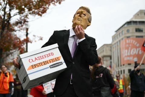 A protester wearing a Trump mask with a Pinocchio nose and carrying a box reading ‘Classified Epstein Files’