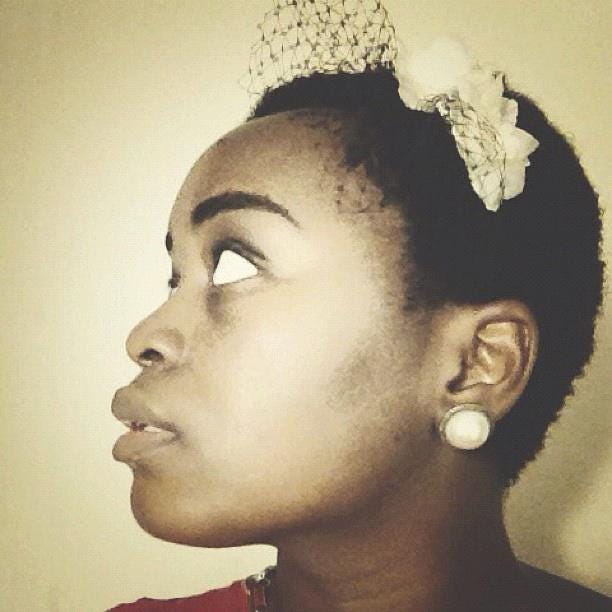 On the left, a profile, of myself from facing the left, eyes looking up in sepia. My hair is a short fro, with flowers and a short veil attached, my earring is a round vintage style. The light is coming from the front on, though shadows lightly circle the image. On the right is my profile in the opposite direction. The image is in full color and the light pours in from the right onto my downcast face, with tones of purple and orange. I am wearing an orange shirt, and my locs are tied up with an orange scrunchie. There is an african printed orage, green, and red cloth used as a headband around my head. The center of the photo is a gold earring in the shape of the main continent of Africa.