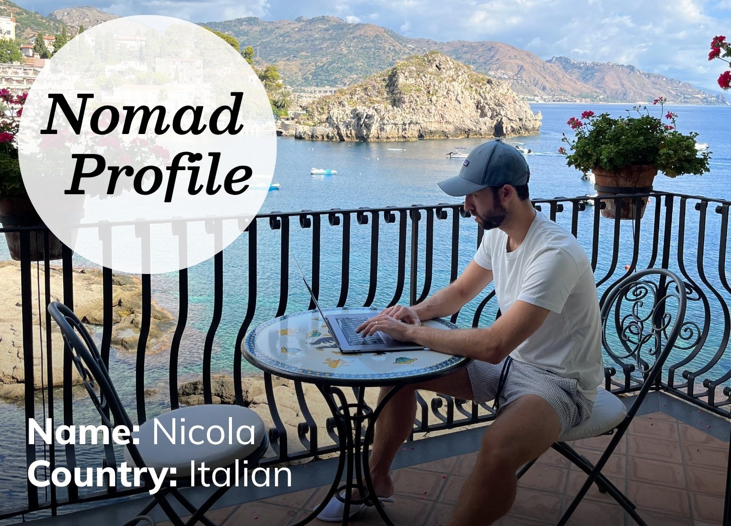 A white man wearing a baseball cap and t-shirt is sitting outside on a balcony working on a laptop. In the background is a dramatic view of mountains and the sea.