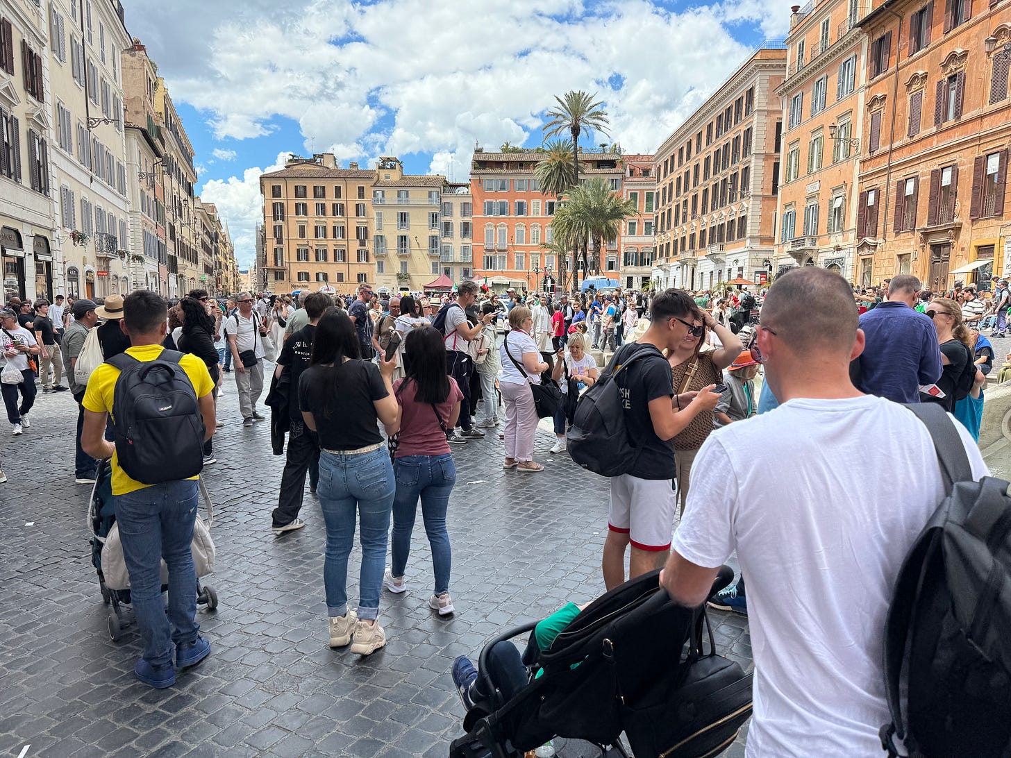 tourists in large piazza in Rome surrounded by stucco buildings, pastel colors
