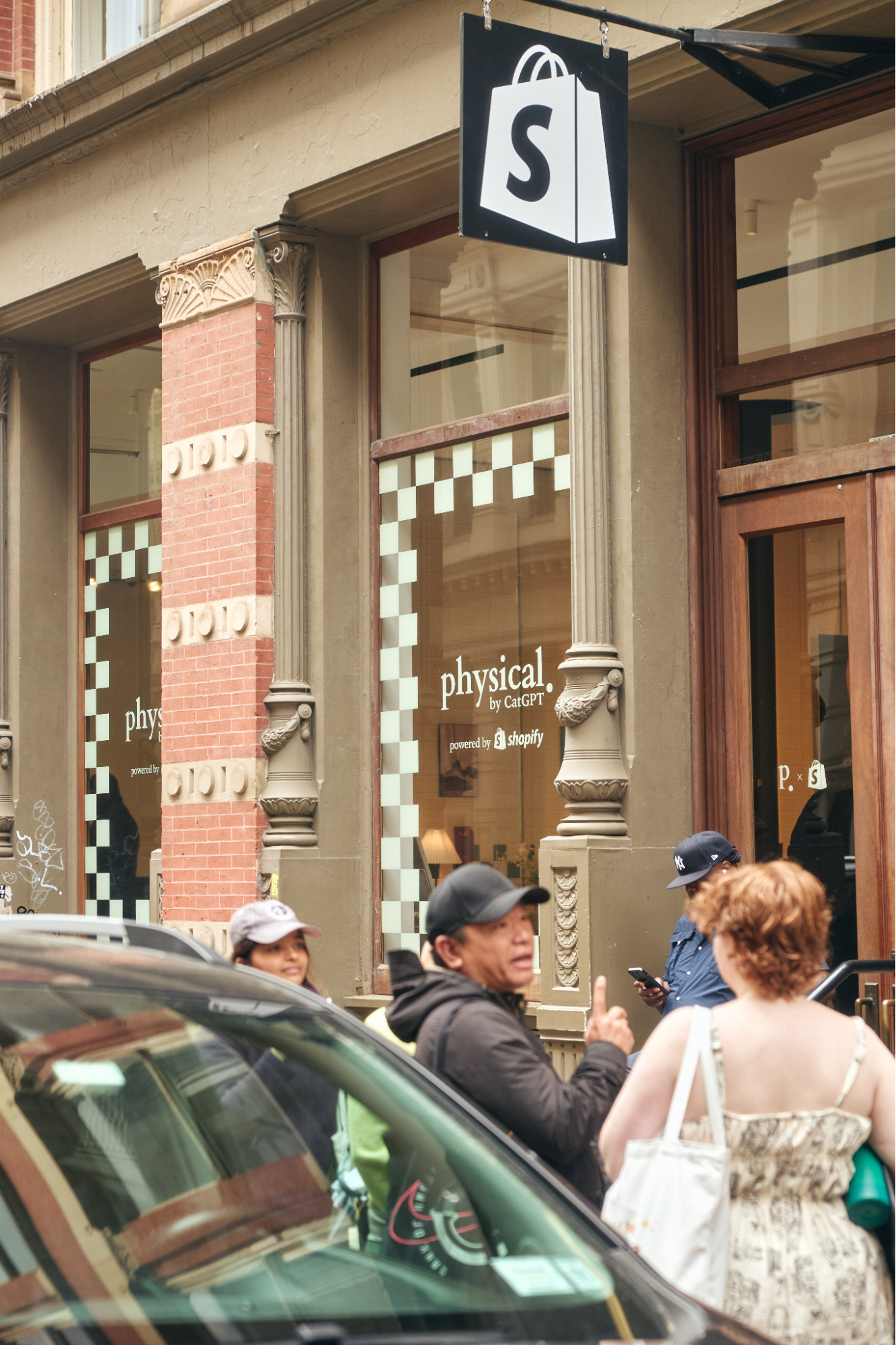 Shopify Space exterior. Windows read "physical. by CatGPT powered by Shopify." Pedestrians stand on the sidewalk.