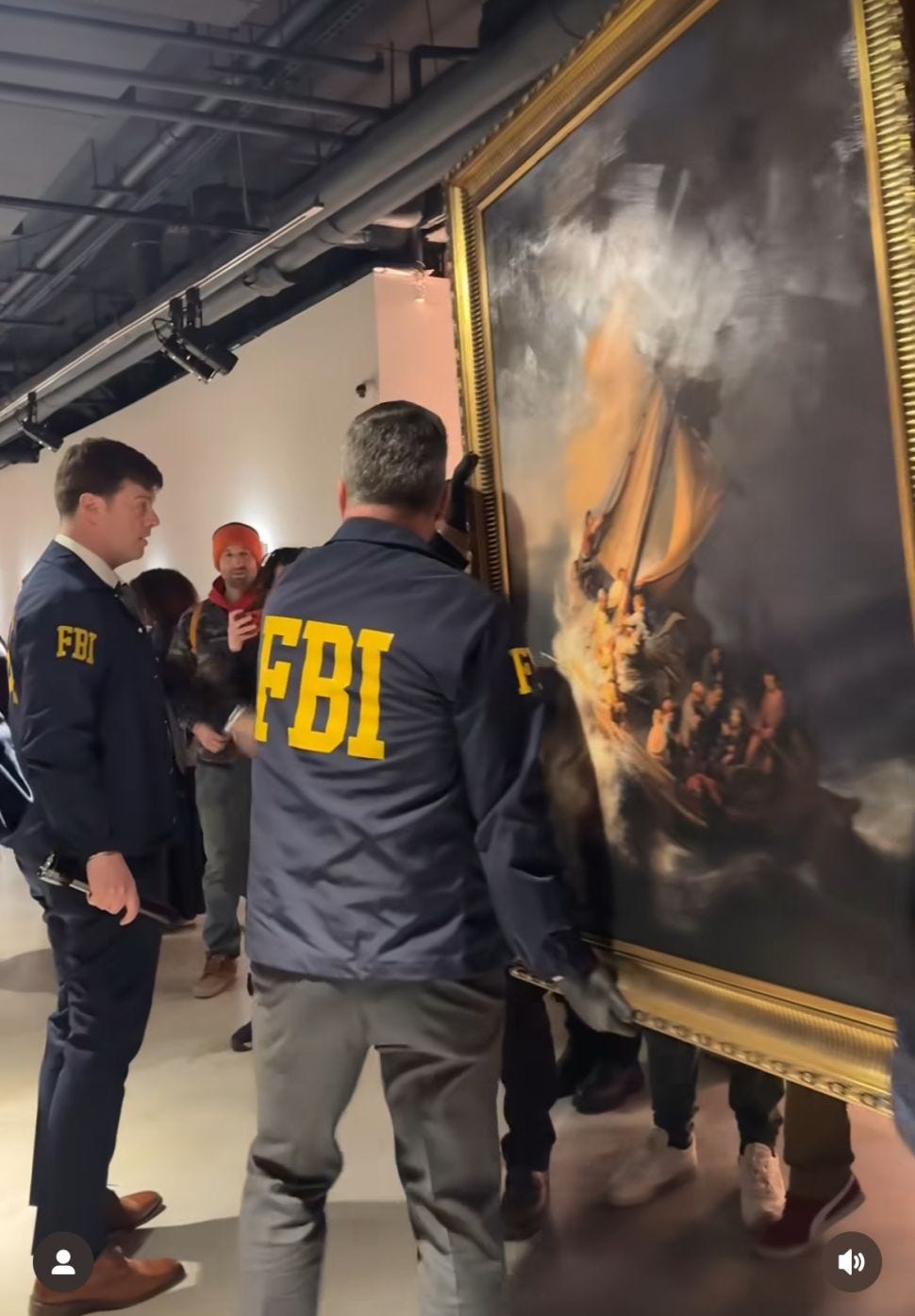 Two men dressed with FBI jackets hold a painting to take it out of a gallery