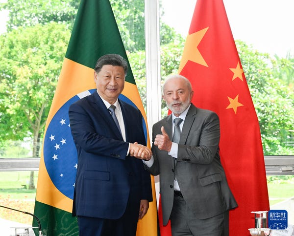 Chinese President Xi Jinping and Brazil's president shake hands before the national flags of Brazil and China.