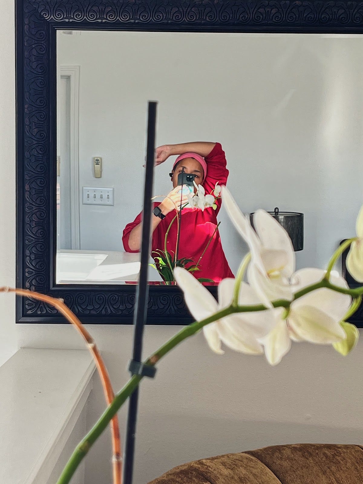 A girl in a pink silk scarf and red sweatshirt looking taking a photo of herself in the mirror