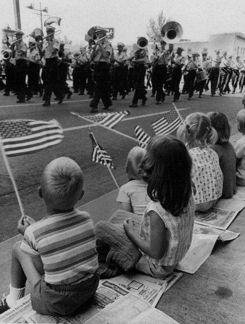 This may contain: a group of children sitting on the ground watching a parade
