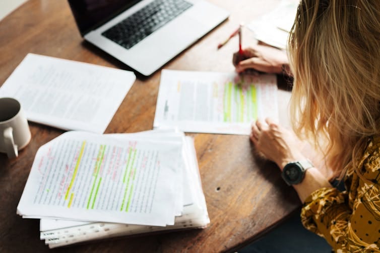 high angle of woman marking papers with laptop in background high angle of woman marking papers with laptop in background