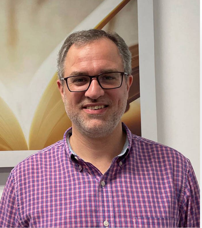 Portrait of Marcus Wengerd, a man in glasses and a purple plaid shirt in front of a floral backdrop. Portrait of Marcus Wengerd, a man in glasses and a purple plaid shirt in front of a floral backdrop.
