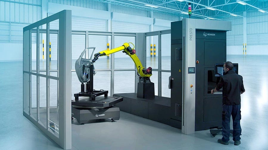 A person operates a large industrial machine with a yellow robotic arm handling a car door in a spacious, well-lit industrial setting. A person operates a large industrial machine with a yellow robotic arm handling a car door in a spacious, well-lit industrial setting.