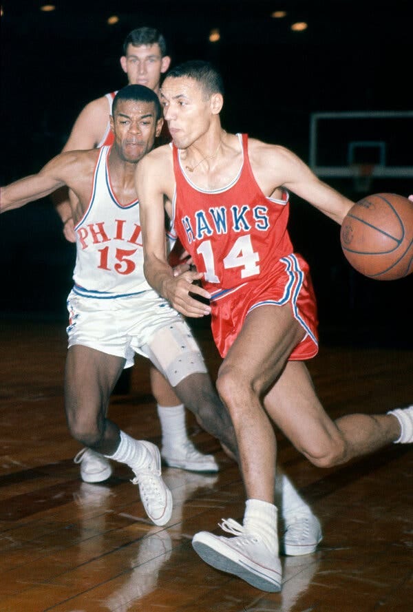 A man in red shorts and shirt dribbles a basketball past another player. A man in red shorts and shirt dribbles a basketball past another player.