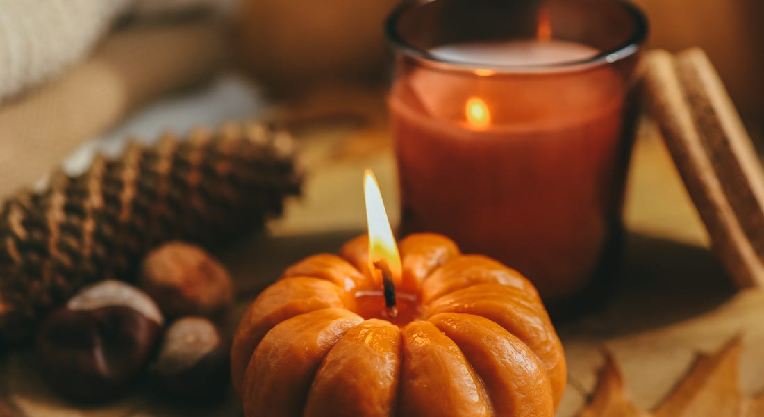 An orange pumpkin candle next to a brown glass candle, with pinecones and conkers around it An orange pumpkin candle next to a brown glass candle, with pinecones and conkers around it