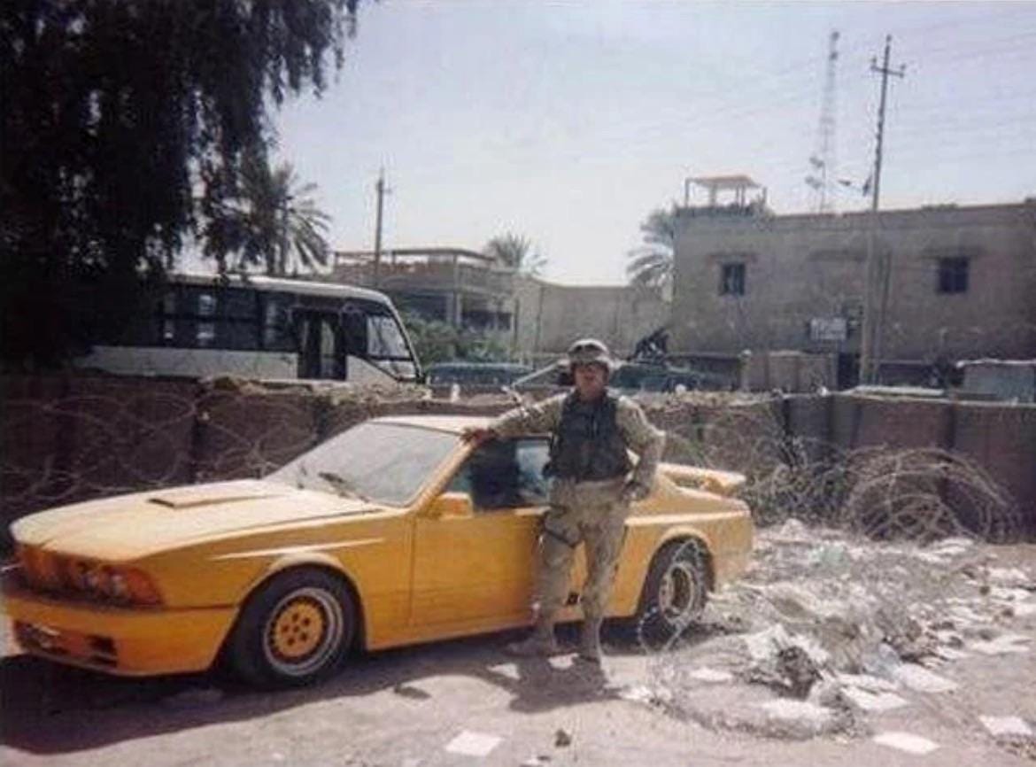 A U.S. soldier next to a distinctive yellow 1985 BMW 635CSi, modified by Gemballa, photographed after the Fall of Baghdad and invasion of Iraq, circa April-May 2003.