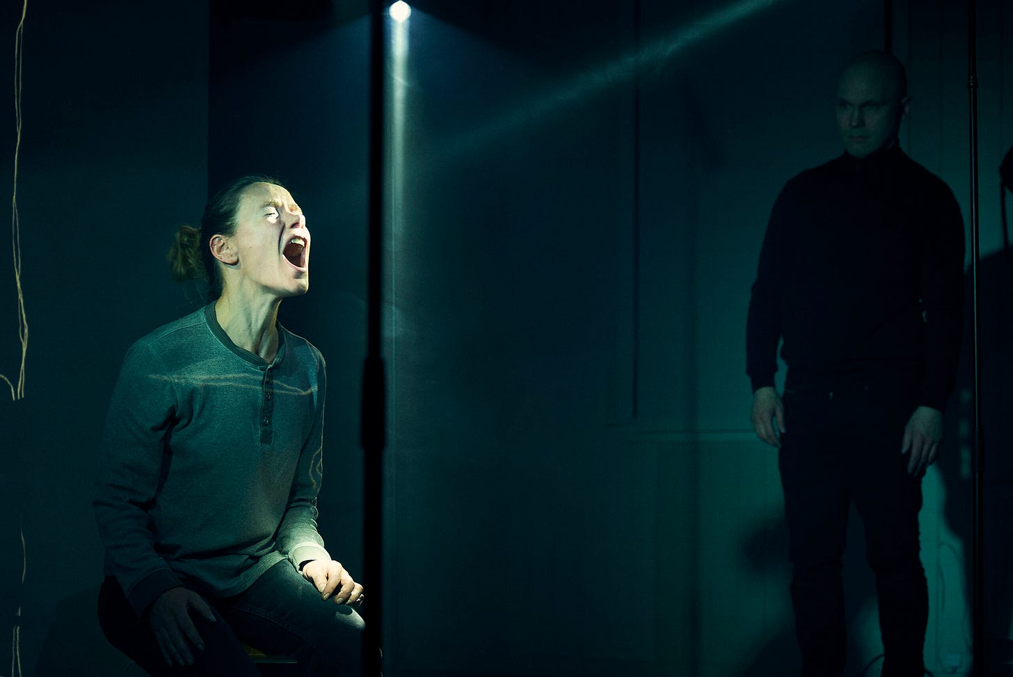 A woman stands with her mouth open as if to scream while a man looks on.