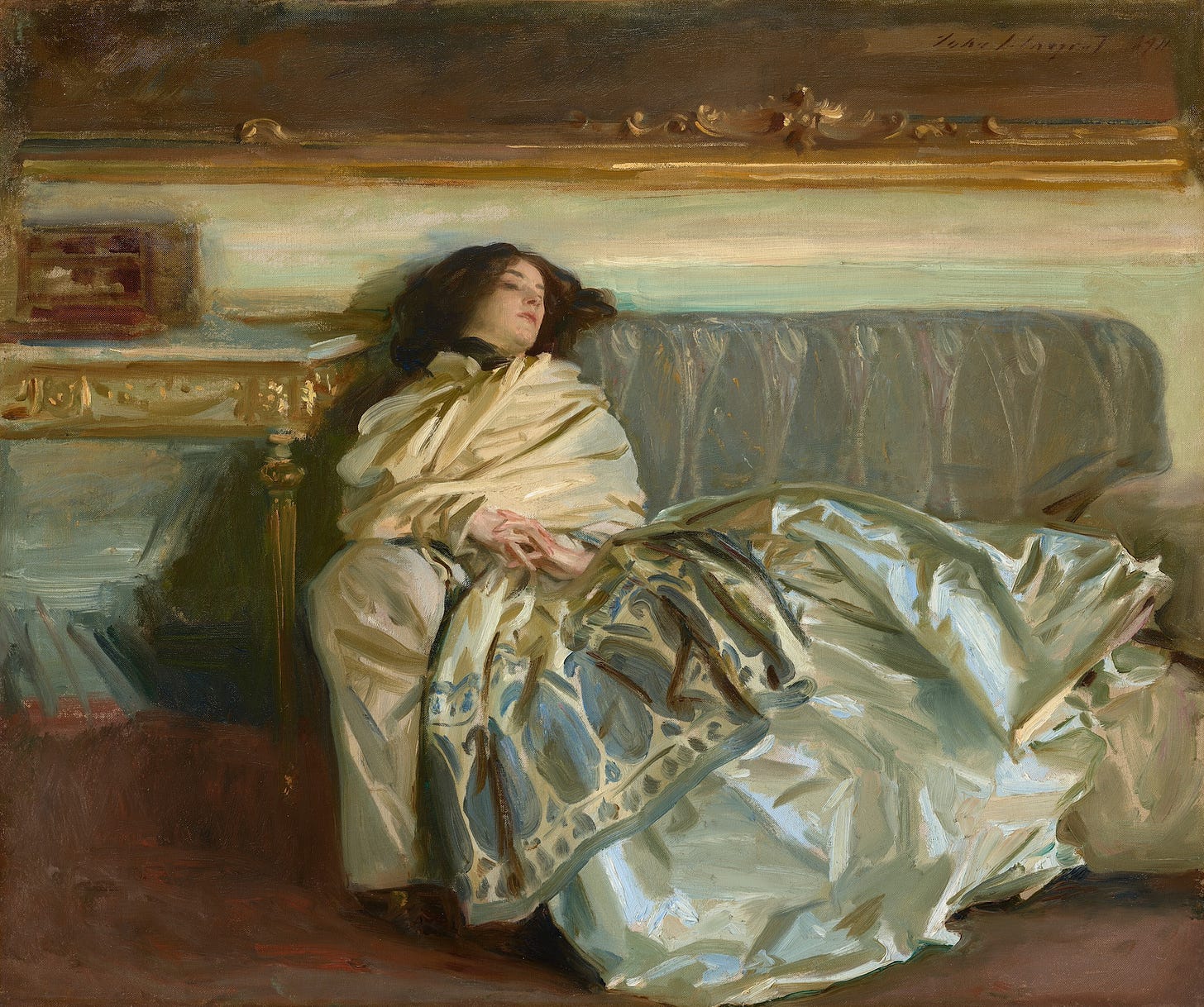 A woman with pale skin and dark brown hair is swathed in silky fabric as she reclines along a gray couch in this horizontal painting. Her head rests along the backrest of the sofa to our left, so her body extends to our right. Her torso is wrapped in a voluminous, ivory-white scarf or wrap. The scarf wraps tightly around her neck, and the bottom edge, near her knees, has a wide, indigo-blue pattern of ovals and vegetal forms. Her shimmering silver gray skirt is painted loosely with baby and sky blue, olive and sage green, and white strokes, and it drapes over the cushions and down the front of the couch. Her hands are clasped so her interwoven fingers rest at her navel. She looks down and off to our right. A table to our left is edged with gold. The wall behind her, above the couch, is painted with long streaks of eggshell white and pale turquoise. The gold frame of a dark painting hanging over the couch spans the width of the composition. Near the upper right corner of the canvas, the artist included a signature and as if he had signed the painting within this painting with loose, dark letters: “John S. Sargent 1911.” A woman with pale skin and dark brown hair is swathed in silky fabric as she reclines along a gray couch in this horizontal painting. Her head rests along the backrest of the sofa to our left, so her body extends to our right. Her torso is wrapped in a voluminous, ivory-white scarf or wrap. The scarf wraps tightly around her neck, and the bottom edge, near her knees, has a wide, indigo-blue pattern of ovals and vegetal forms. Her shimmering silver gray skirt is painted loosely with baby and sky blue, olive and sage green, and white strokes, and it drapes over the cushions and down the front of the couch. Her hands are clasped so her interwoven fingers rest at her navel. She looks down and off to our right. A table to our left is edged with gold. The wall behind her, above the couch, is painted with long streaks of eggshell white and pale turquoise. The gold frame of a dark painting hanging over the couch spans the width of the composition. Near the upper right corner of the canvas, the artist included a signature and as if he had signed the painting within this painting with loose, dark letters: “John S. Sargent 1911.”