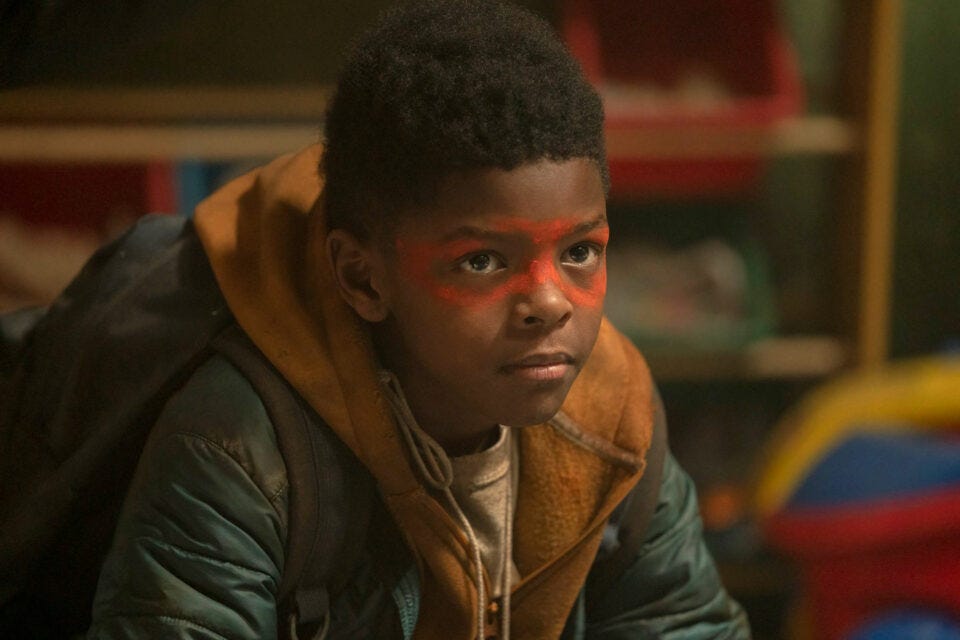 A Black Deaf boy wears a superhero’s mask, painted on his face.