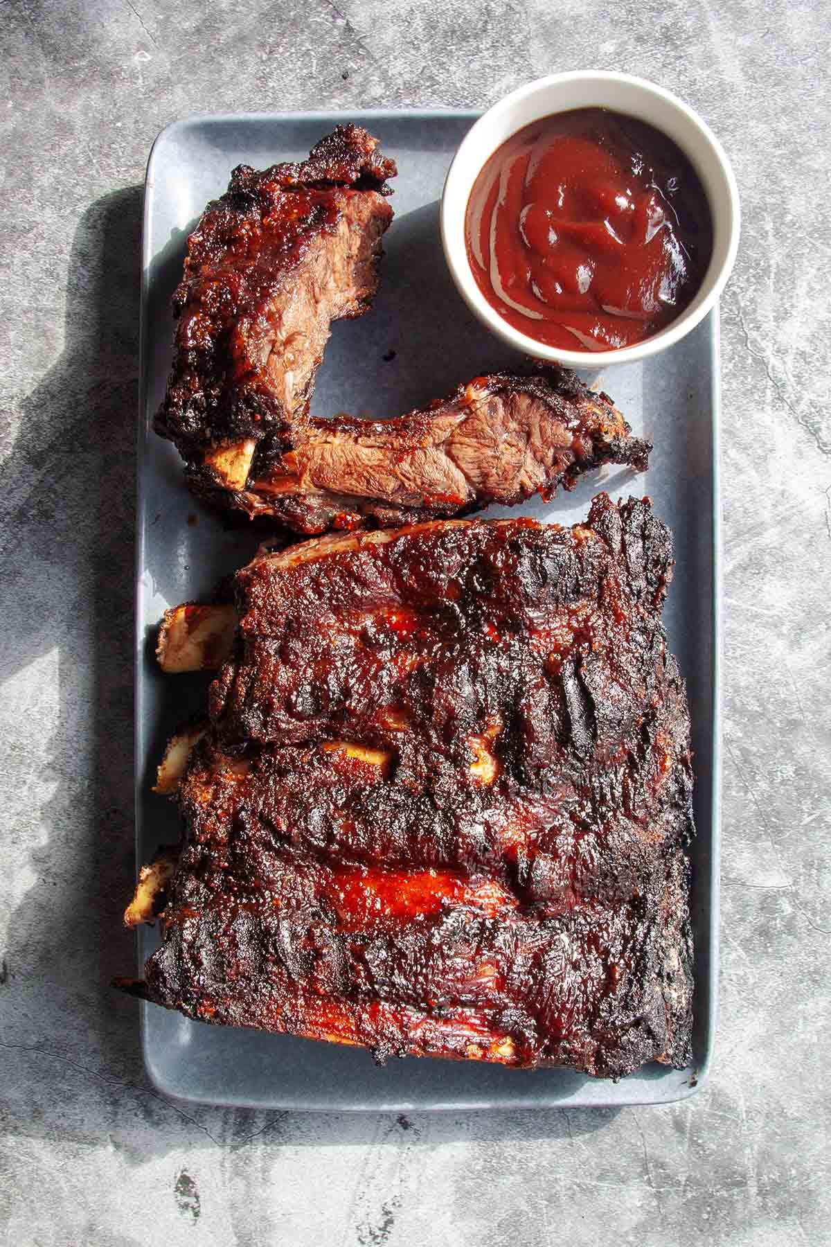 A stack of tender, slow-grilled barbecued beef back ribs on a platter with visible smoky char and spice rub.
