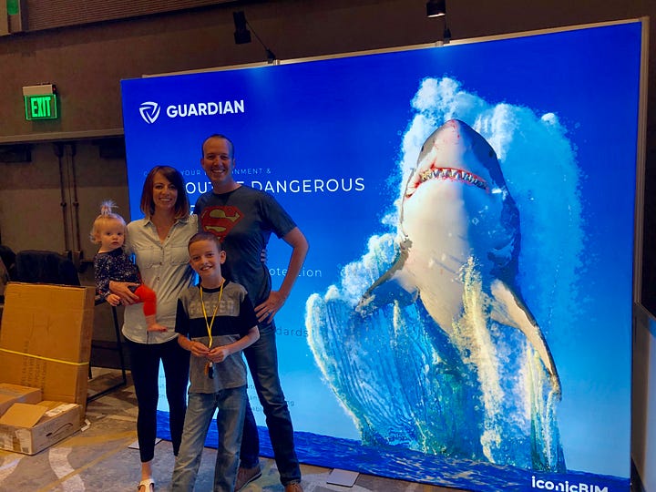 Family helping Parley set up booth at a conference. The booth backdrop is of a shark and says "Stay out of dangerous waters."