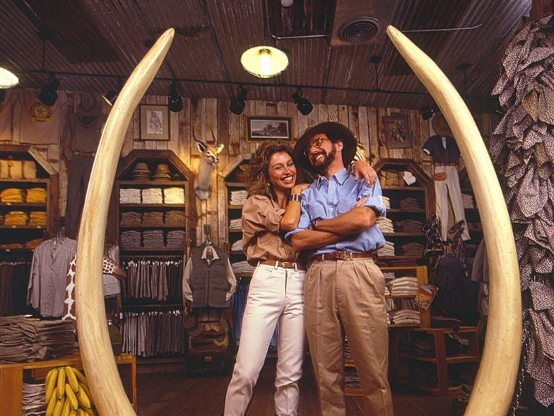 Two people standing in a clothing store featuring taxidermy and two large elephant's tusks