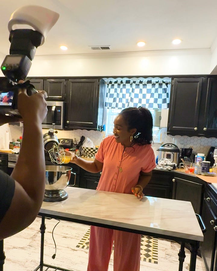 Behind-the-scenes of The Soul Food Pot® cookbook photoshoot showing Shaunda Necole mixing ingredients in a home kitchen while being filmed, capturing modern soul food recipe creation and storytelling