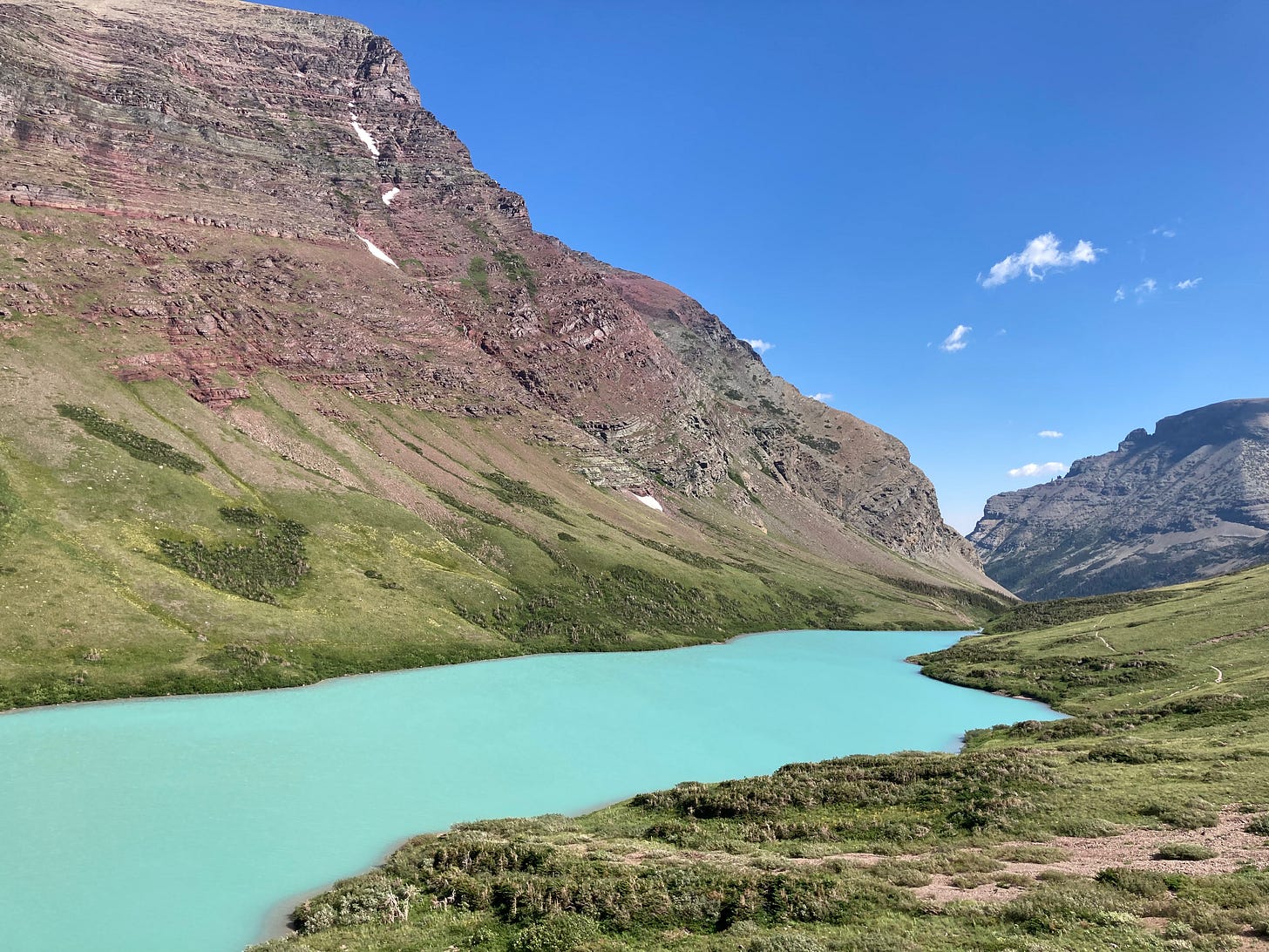A vibrant glacial silt lake appears turquoise sitting under walls of red tinged rock. A vibrant glacial silt lake appears turquoise sitting under walls of red tinged rock.