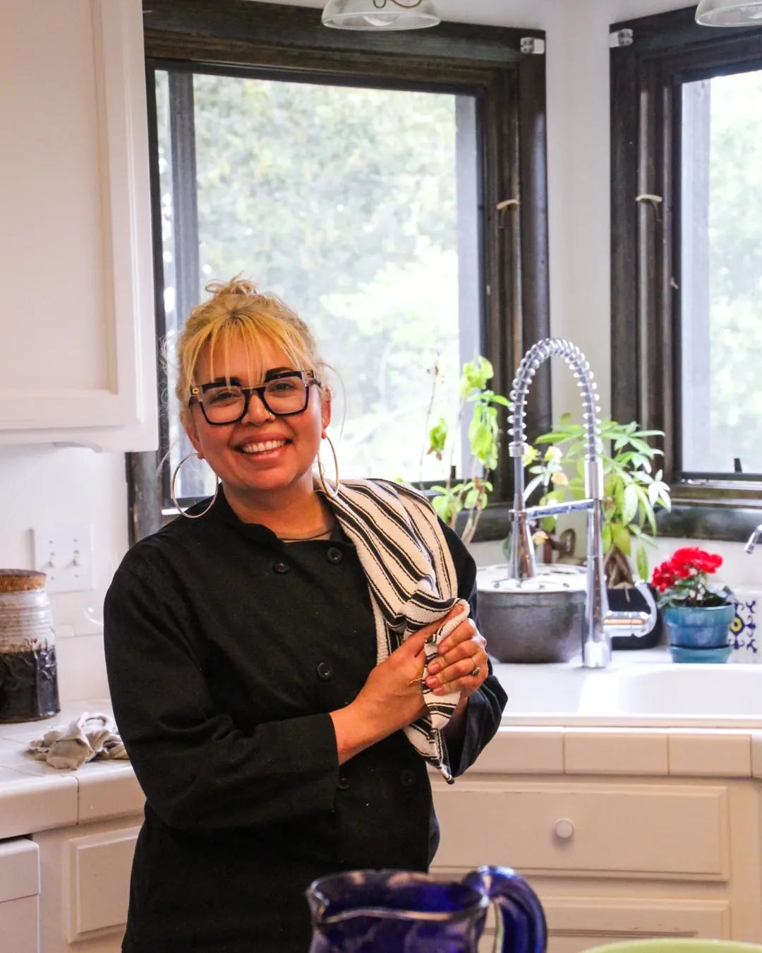 Chef Candice, a latina woman in her mid-30s, smiles directly at the camera. She stands in a white kitchen. 