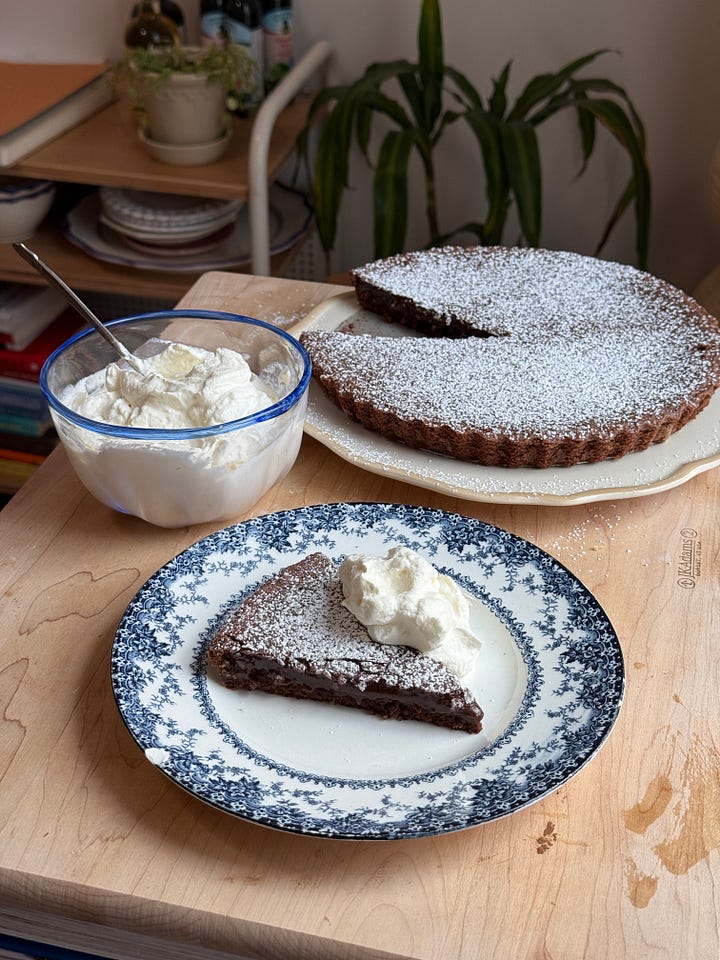 a kladdkaka with a slice on a plate next to a bowl of whipped cream