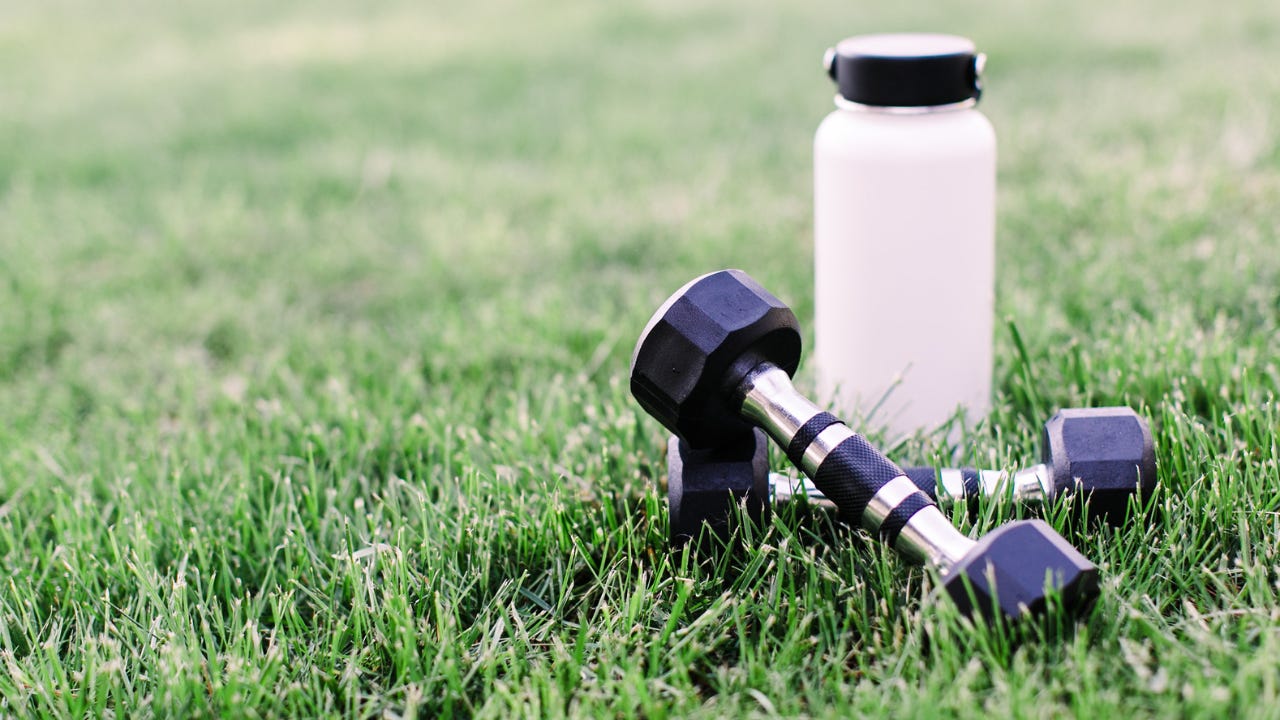 Black dumbbells and a white water bottle resting on green grass outdoors. Black dumbbells and a white water bottle resting on green grass outdoors.