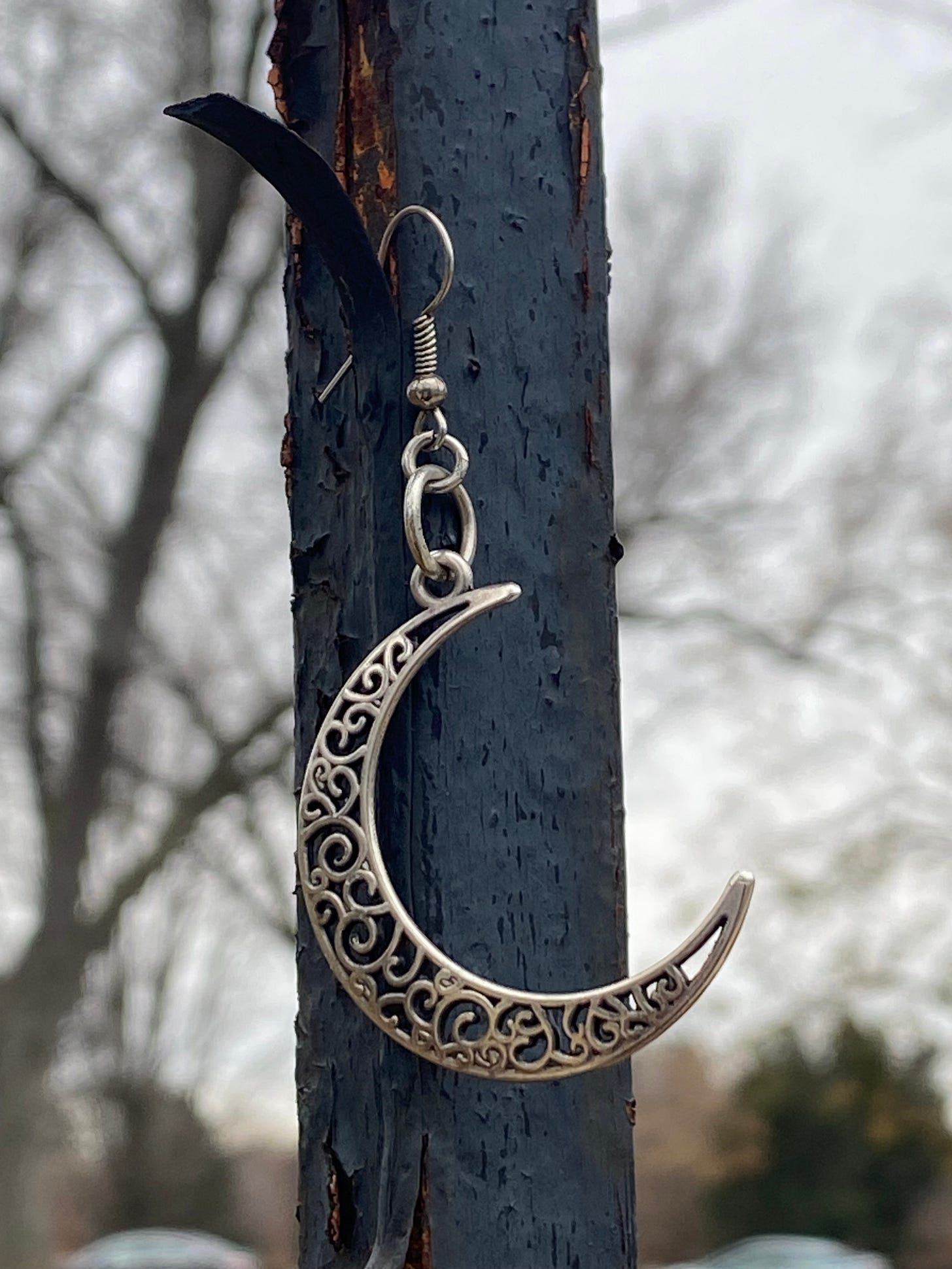 A silver crescent moon earring hanging on a fence