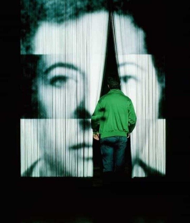 This may contain: a man standing in front of a large screen with a woman's face on it