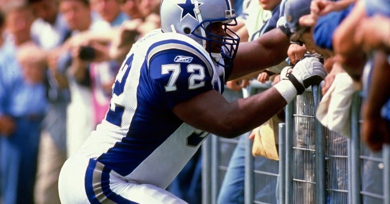 A photograph of an NFL player in action, pushing against a barrier with spectators in a stadium. A photograph of an NFL player in action, pushing against a barrier with spectators in a stadium.