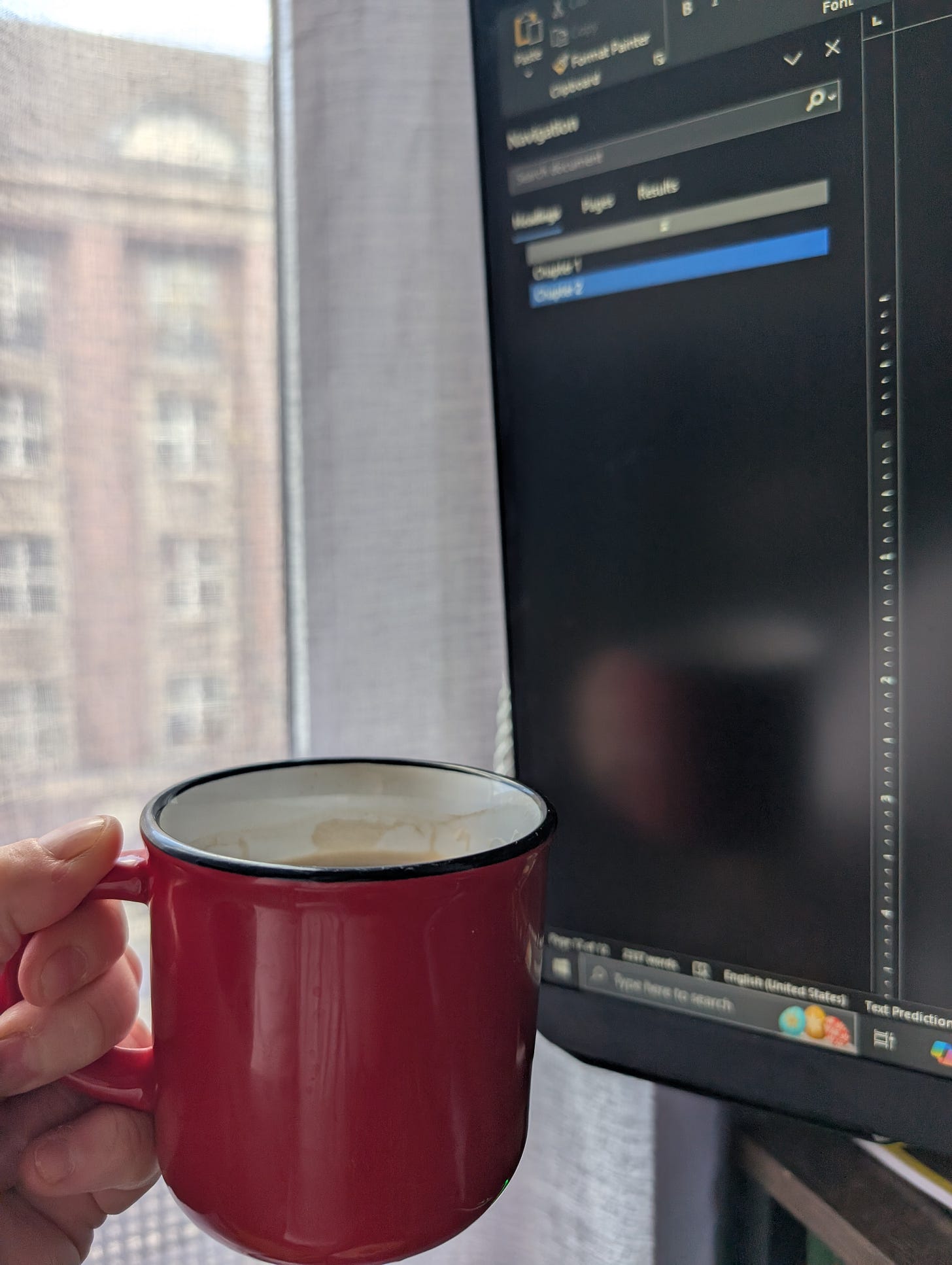 A close-cropped photo of my hand holding a red coffee mug in front of a blurred computer screen with a word document open, showing “Chapter 1” and “Chapter 2” in the outline of the document.