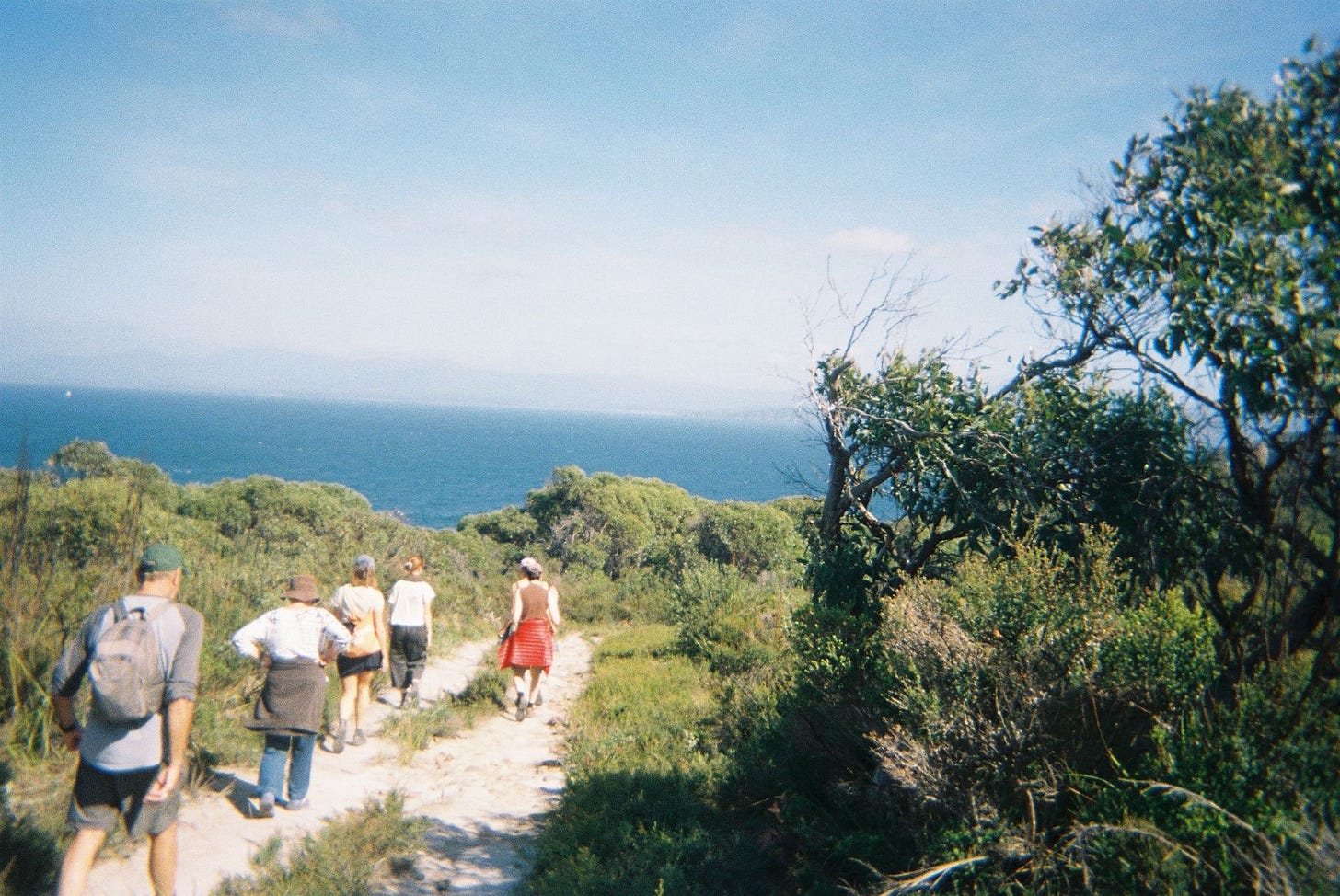 A family of adults walk on a natural trail towards the ocean in the distance.