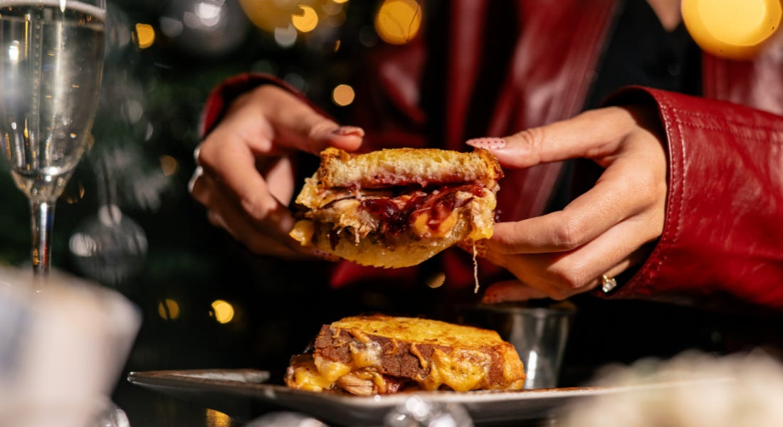 A person wearing a red jacket holding a cheese toastie, with fairy lights and disco balls around them