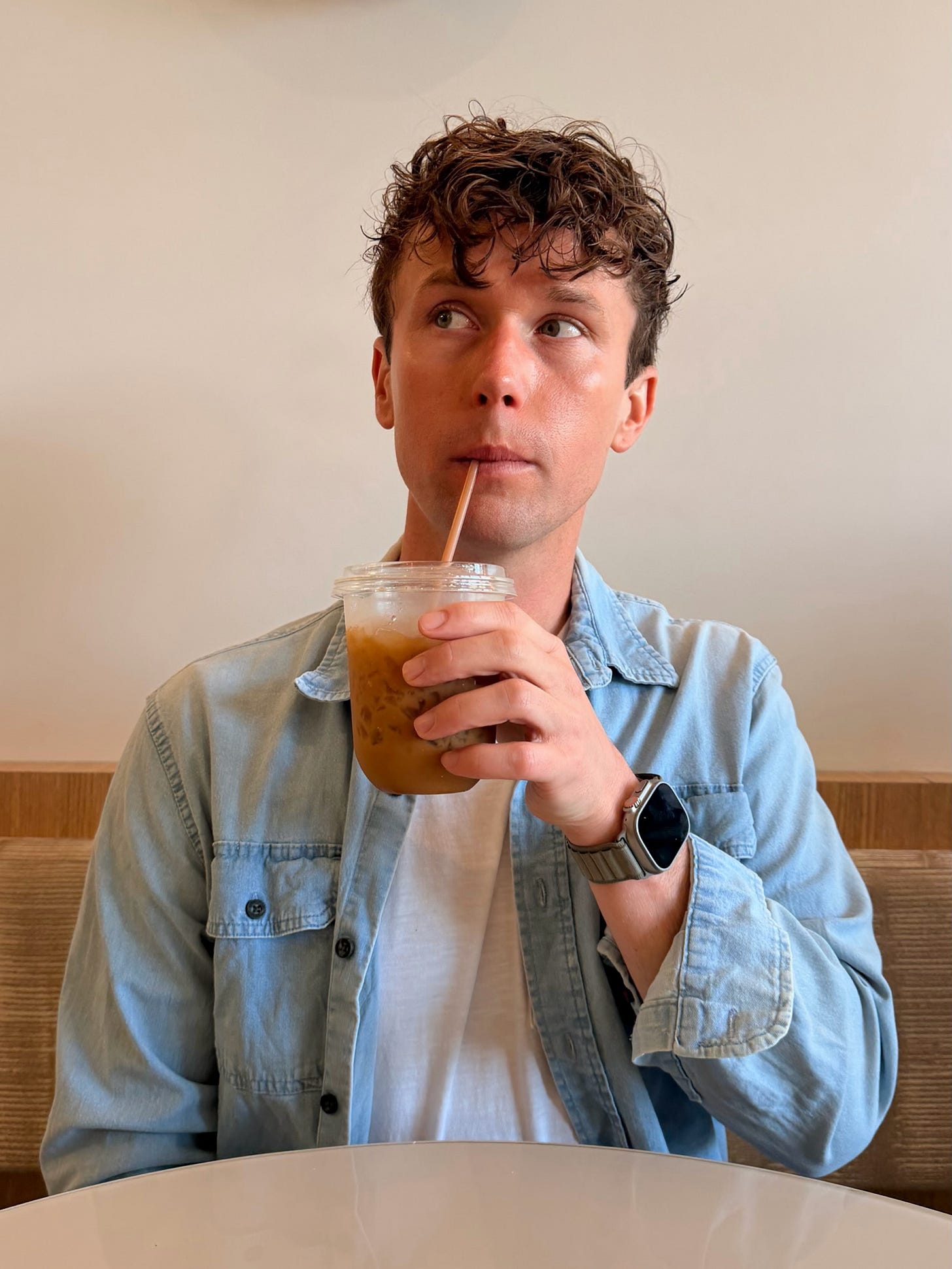 Levi Chambers sipping an iced drink at a café, wearing a light blue denim shirt. Levi Chambers sipping an iced drink at a café, wearing a light blue denim shirt.