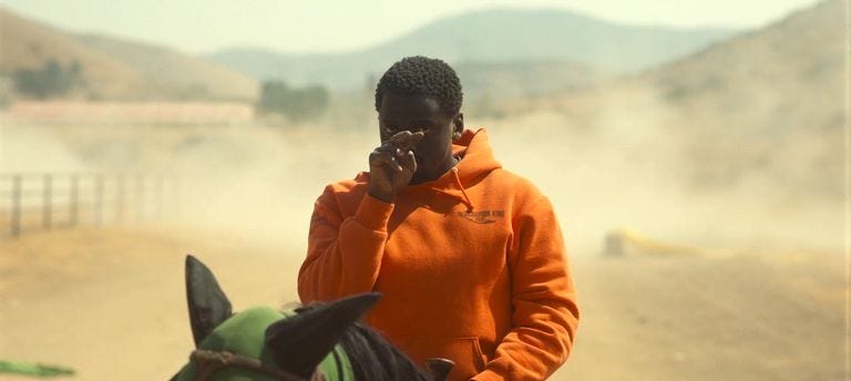OJ on a horse looking towards the camera with his index finger and middle finger pointing from his eyes towards our eyes.