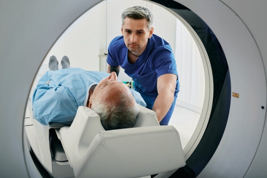 Male health provider helps a older male patient into a MRI machine