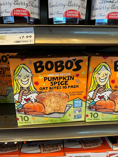 A grid of six photos of pumpkin-flavored products on shelves at an American Whole Foods: pumpkin spice grain-free cereal, pumpkin spice popcorn, pumpkin spice oat milk, cans of pumpkin chai hard tea, pumpkin spice oat bites and a pumpkin almond flour pancake mix.
