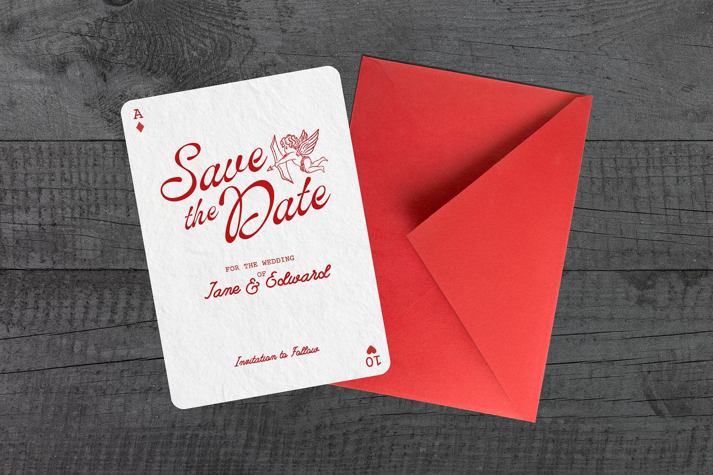 A top-down view on dark grey wood showing a bright red envelope next to a custom "Save the Date" card. The card features red typography reading "Save the Date for the wedding of Jane & Edward" alongside an illustration of Cupid.